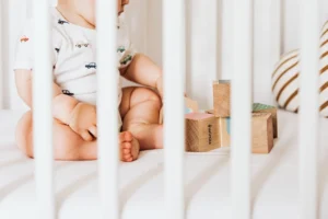Een baby in de box die nog niet doorslaapt maar aan het spelen is met blokken.